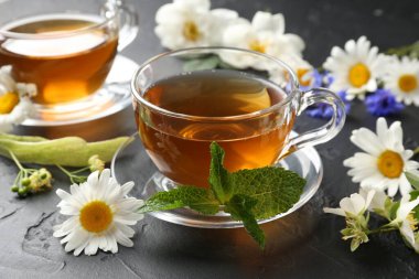 Cam bardaklarda romatik bitki çayı, farklı çiçekler ve siyah masada nane şekeri, yakın plan.