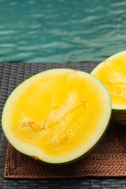 Yüzme havuzunun yakınındaki hasır masada olgun sarı karpuz parçaları.