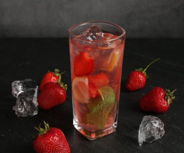 Çilekli içecek ve koyu dokulu masa üzerindeki buz gri arka planda, yakın plan.