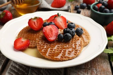 Lezzetli Hollanda Waffle 'ları (stroopwafels) bal, çilek ve böğürtlen ile ahşap masada, yakın plan