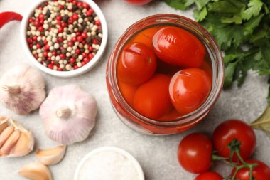 Kavanozda lezzetli domates turşusu ve açık gri masada malzemeler.