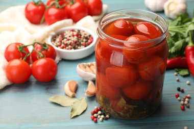 Kavanozda domates turşusu ve açık mavi ahşap masada malzemeler, yakın plan.