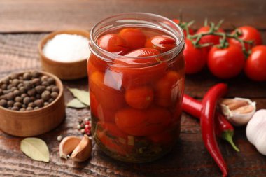 Kavanozda salamura domates ve ahşap masada malzemeler, yakın plan.