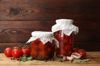 Kavanozlarda salamura domates, taze ürünler ve ahşap masada baharatlar, yakın plan.