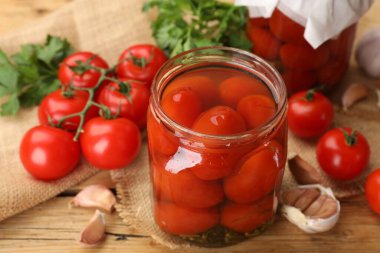 Kavanozda lezzetli domates turşusu, taze olanlar ve ahşap masada sarımsak, yakın plan.