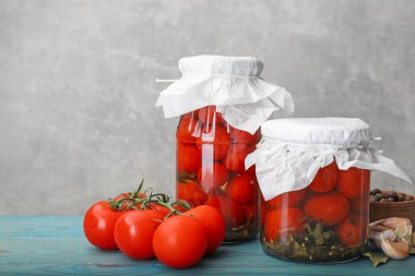 Kavanozlarda salamura domates, taze ürünler ve baharatlar açık mavi ahşap masa üzerinde gri arka plan, yakın plan