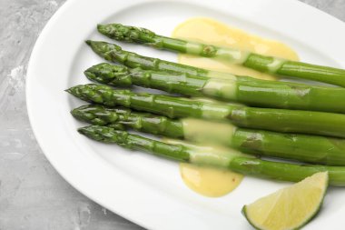 Sos ve limonla servis edilen lezzetli pişmiş kuşkonmaz. Gri desenli masa, üst manzara.