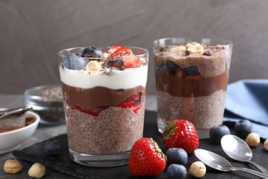 Chia tohumlu, fındıklı ve böğürtlenli lezzetli çikolatalı pudingler gri masada, yakın plan.