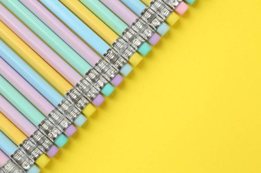 Sarı arka planda silgisi olan bir sürü grafit kalem, düz bir zemin. Metin için boşluk