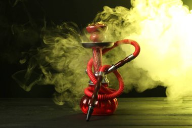 Siyah arka planda sigara dumanı olan ahşap masada nargile.