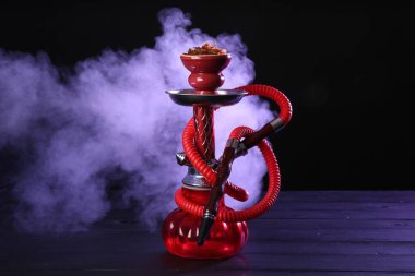 Siyah arka planda sigara dumanı olan ahşap masada nargile.