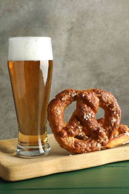 Lezzetli krakerler ve yeşil ahşap masada bir bardak bira. Gri desenli arka plan, yakın plan.