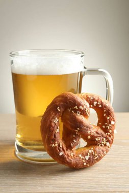 Lezzetli kraker ve bir bardak bira ahşap masada, gri arka planda, yakın planda.