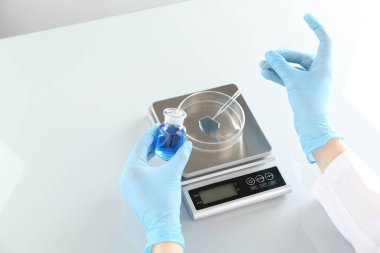 Laboratuvardaki beyaz ayna masasında numune ve terazilerle çalışan bilim adamı.