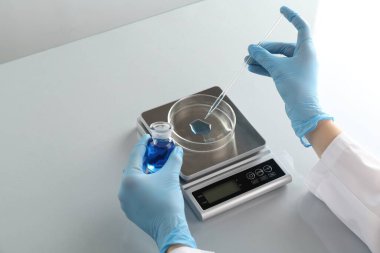 Laboratuvardaki beyaz ayna masasında numune ve terazilerle çalışan bilim adamı.