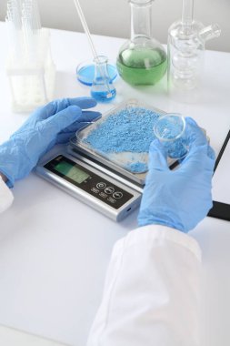 Bilim adamı beyaz masadaki terazide numune tartıyor, yakın plan.