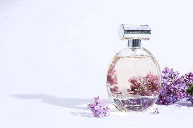 Parfüm şişesi ve açık gri arka planda leylak çiçekli dal, yakın plan. Metin için boşluk
