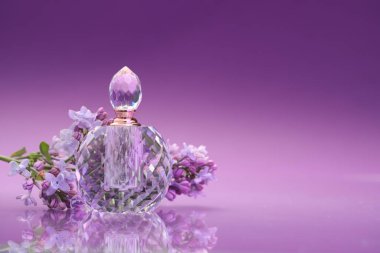 Bir şişe parfüm ve ayna yüzeyinde leylak çiçekleri olan bir dal. Renk eğilimli arka plan, yakın plan. Metin için boşluk