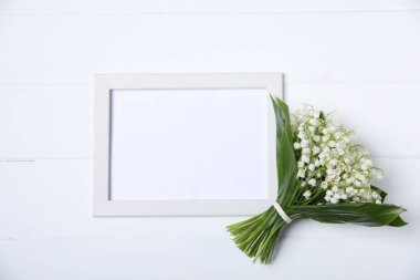 Bir buket güzel vadi zambağı ve beyaz ahşap zemin üzerinde boş çerçeve, üst manzara. Metin için boşluk