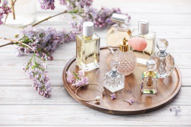 Beyaz ahşap masada parfüm şişeleri ve leylak çiçekleri.