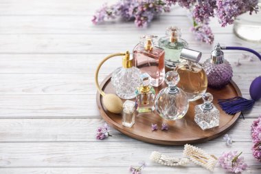 Beyaz ahşap masada parfüm şişeleri, aksesuarlar ve leylak çiçekleri. Metin için boşluk