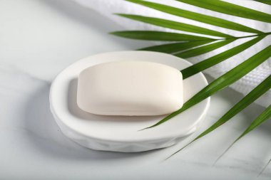 Sabun çubuğu, havlu ve palmiye yaprağı beyaz mermer masada, yakın plan.