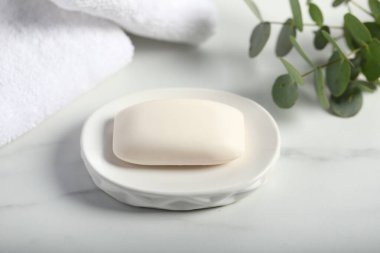 Sabun çubuğu, havlu ve okaliptüs dalları beyaz mermer masa üzerinde, yakın plan.