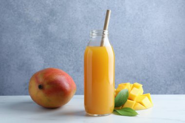 Cam şişede lezzetli mango suyu, taze meyve ve beyaz mermer masada yeşil yapraklar.