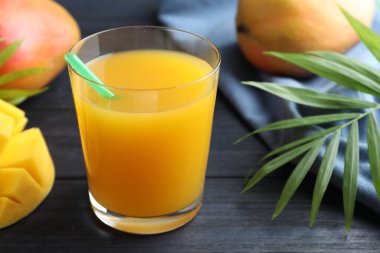 Bardakta lezzetli mango suyu, taze meyve ve ahşap masada yeşil yapraklar, yakın plan.