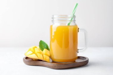 Cam mason kavanozunda lezzetli mango suyu, taze meyve ve beyaz masada nane.