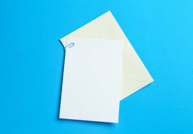 Açık mavi arka planda boş davetiye ve zarf, üst manzara. Tasarım için boşluk