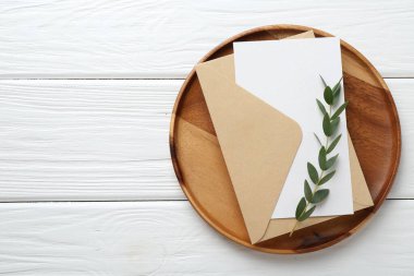 Boş davetiye kartı, zarf, tepsi ve dal beyaz ahşap masa, üst manzara. Metin için boşluk