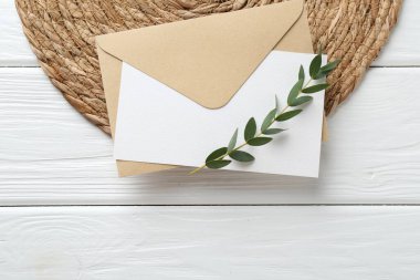 Boş davetiye kartı, zarf, dal ve hasır kaplama beyaz ahşap masa, üst manzara. Metin için boşluk