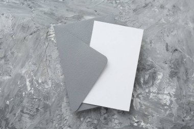 Gri desenli masa üzerinde boş davetiye ve zarf, üst manzara. Metin için boşluk