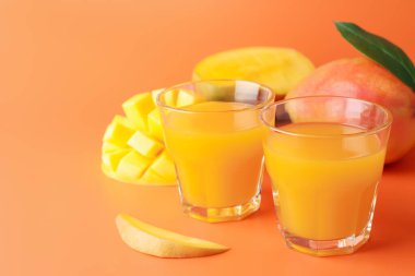 Bardakta lezzetli mango suyu ve turuncu arka planda taze meyve, yakın plan. Metin için boşluk