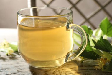 Fincanda taze ıhlamur çayı ve ahşap masada çiçekler, yakın plan.