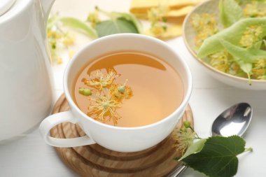 Fincanda taze ıhlamur çayı ve beyaz ahşap masada çiçekler, yakın plan.