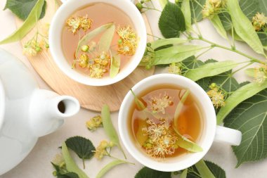 Fincanlarda taze ıhlamur çayı, çaydanlık ve çiçekler beyaz masada, düz yerde.