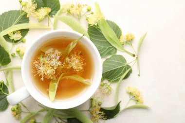 Taze ıhlamur çayı fincanda ve çiçekler beyaz masada, düz yerde.