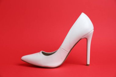 Kırmızı arka planda beyaz topuklu bir ayakkabı.