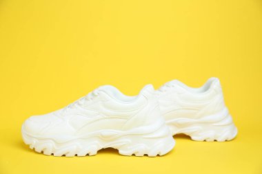 Sarı arka planda bir çift beyaz spor ayakkabı.