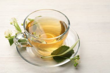 Fincanda taze ıhlamur çayı ve beyaz ahşap masada çiçekler, yakın plan.