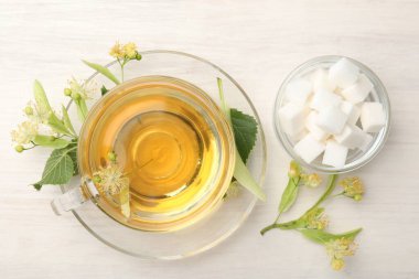 Fincanda taze ıhlamur çayı, küp şekerler ve beyaz ahşap masa üzerinde çiçekler, düz uzanmış