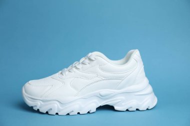 Açık mavi arka planda şık bir beyaz spor ayakkabı.