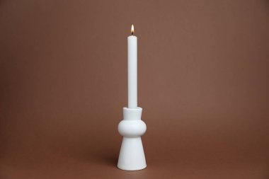 Kahverengi zemin üzerinde yanan mum olan beyaz şamdan