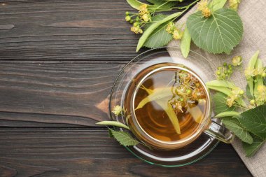 Taze ıhlamur çayı fincanda ve çiçekler koyu ahşap masada, düz yerde. Metin için boşluk