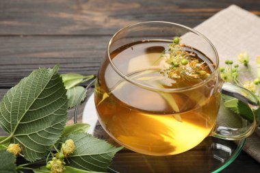 Fincanda taze ıhlamur çayı ve koyu ahşap masada çiçekler, yakın plan.