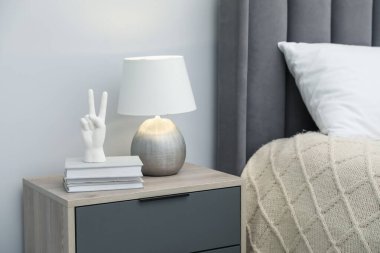 Lamba, el şeklinde beyaz bir figür ve yatağın yanındaki komodinin üzerinde kitaplar.