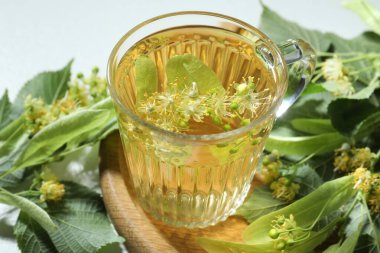 Fincanda lezzetli ıhlamur çayı, ışık masasında yapraklar ve çiçekler, yakın plan.