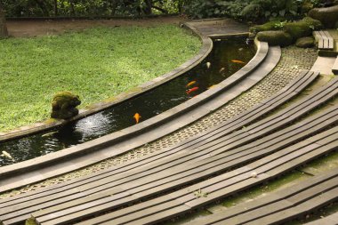 Ahşap banklar, altın balıklı su kanalları ve açık havada yeşil çimenler.